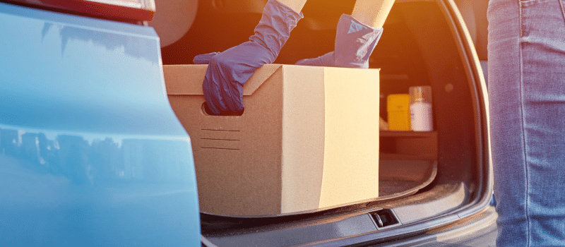 A close up of a car trunk where a person is pulling a box out of the trunk to drop off