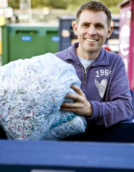 A smiling man holding a clear bag of shredded paper